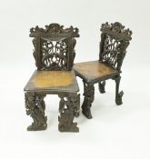 A matched pair of 19th Century Indonesian carved teak hall chairs with figural decoration and