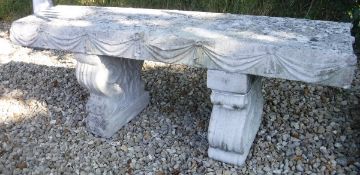 A composite stone garden bench decorated with swags raised on scroll end supports
