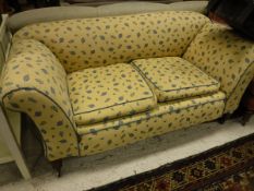 A Victorian drop-arm sofa upholstered in yellow ground and blue leaf patterned fabric,