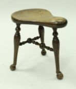 A Victorian mahogany saddle shaped stool, raised on three turned supports to ball feet,