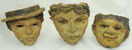 A set of three fired clay wall pockets of facial design,