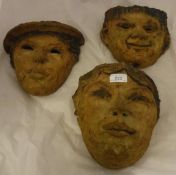 A set of three fired clay wall pockets of facial design,
