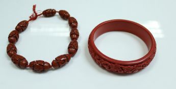 A cinnabar lacquered bead necklace, each bead approx 2 cm long, together with a similar bangle,
