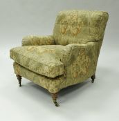 A pair of Howard style armchairs on turned front legs to brass caps and castors,
