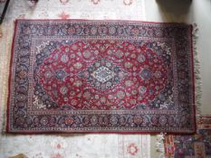 A Kashan medallion rug, the central panel set with floral decorated medallion on a red ground,
