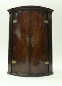 A late George III mahogany hanging corner cupboard of bow fronted form,