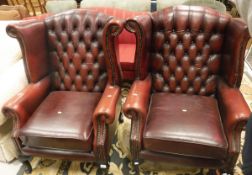 A pair of modern red leather upholstered wing back armchairs with button backs and scroll arms