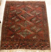 A Turkoman rug, the central panel set with repeating medallions on a dark red ground,