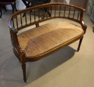 A late Victorian mahogany framed spindleback salon settee with rush seat on turned and fluted front