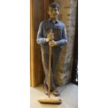 A life-size papier-mache figure of a man in dungarees leaning upon a broom,