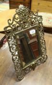 A lacquered brass framed easel mirror with mask and scrolling foliate decoration in teh Rococo