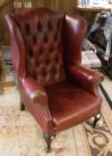 A red buttoned leather wingback scroll armchair on cabriole front legs in the Georgian manner
