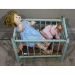 Three plastic dolls and a green painted railed dolls crib,