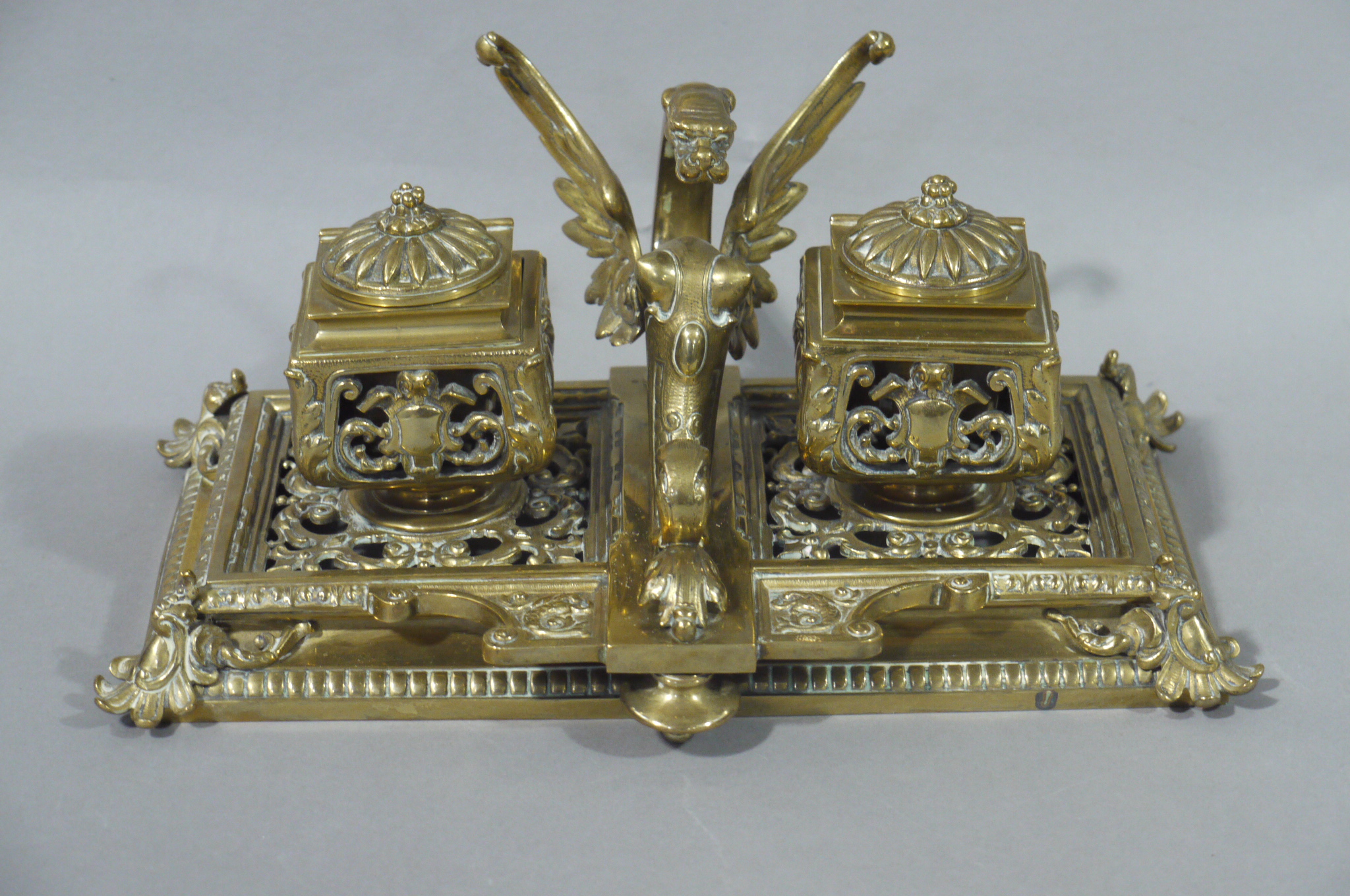 A Victorian brass desk standish having two inkwells and centre griffin pen rest,