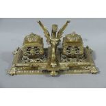 A Victorian brass desk standish having two inkwells and centre griffin pen rest,