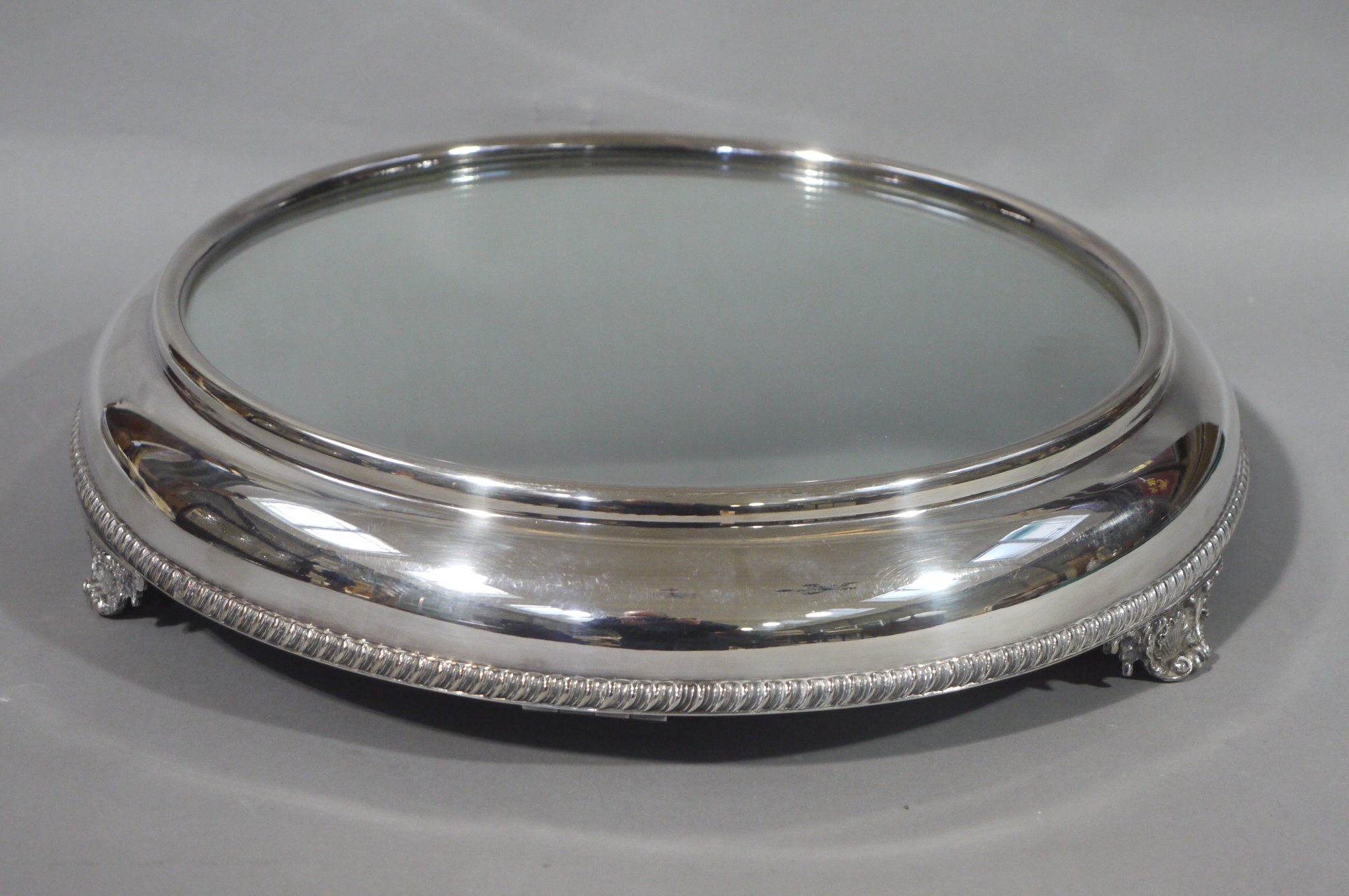 A mirrored silver plate cake stand circular outline with gadroon rim and on shell bracket feet, 37.