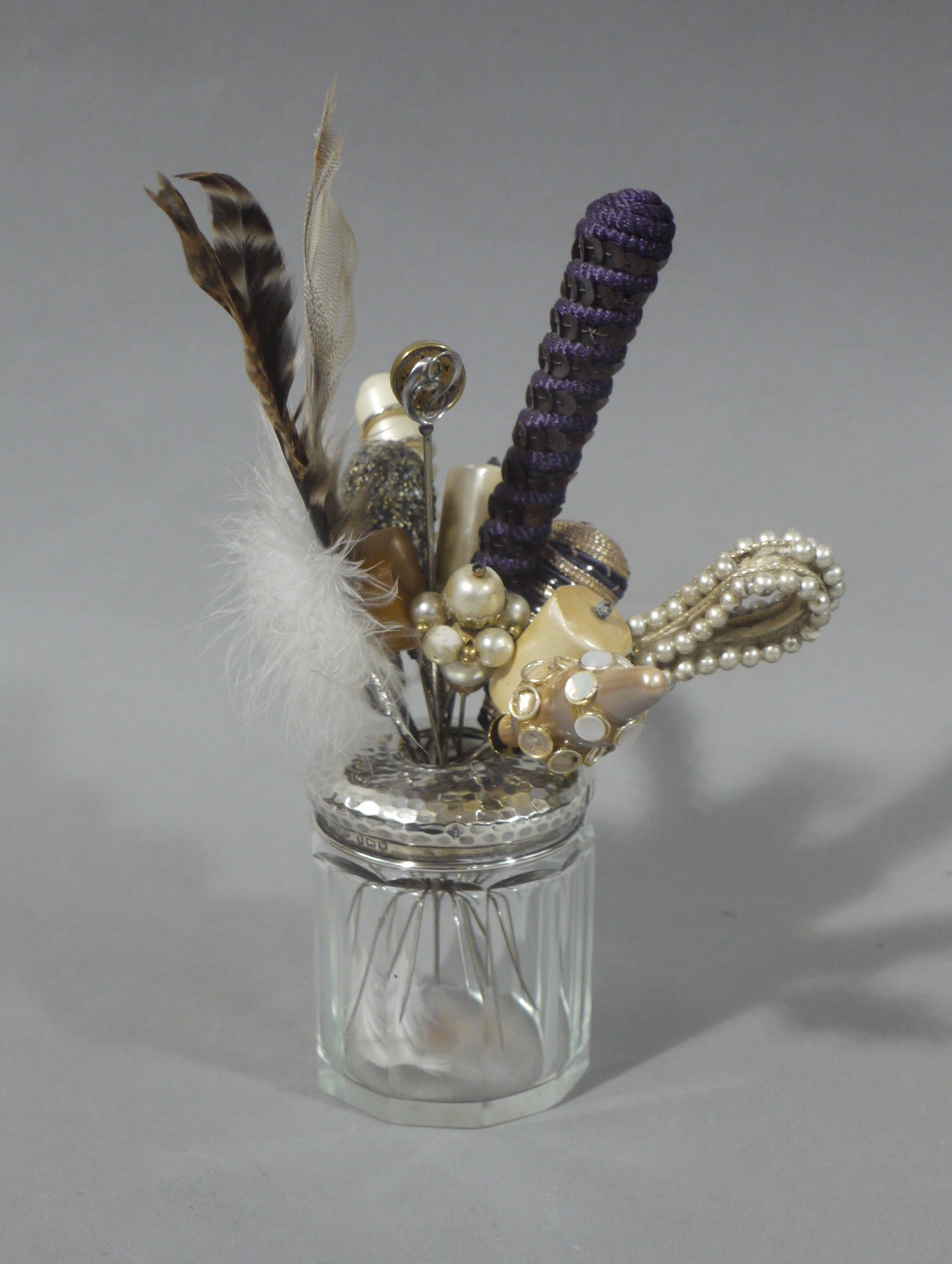 A collection of hat pins held in a silver lidded glass hair tidy