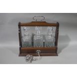 A reproduction mahogany finish three bottle Tantalus with silver plated loop carrying handle