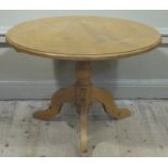 A reproduction pine breakfast table the circular top above a turned column and three flattened