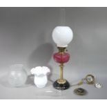 A Victorian oil lamp with cranberry glass reservoir with opaque white glass shade and chimney the