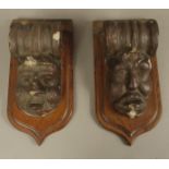 A MATCHED PAIR OF 17TH CENTURY STONE MASK CORBELS with scrolling tops above carved mask caricatures,