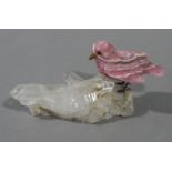 A rose quartz miniature bird resting on a quartz rock,
