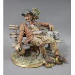 A Naples Capo di Monte figure of a drunken tramp seated on a bench with satchel to his left,