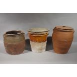 Three terracotta storage jars or crocks, one with cover, one with wooden lid, one without,