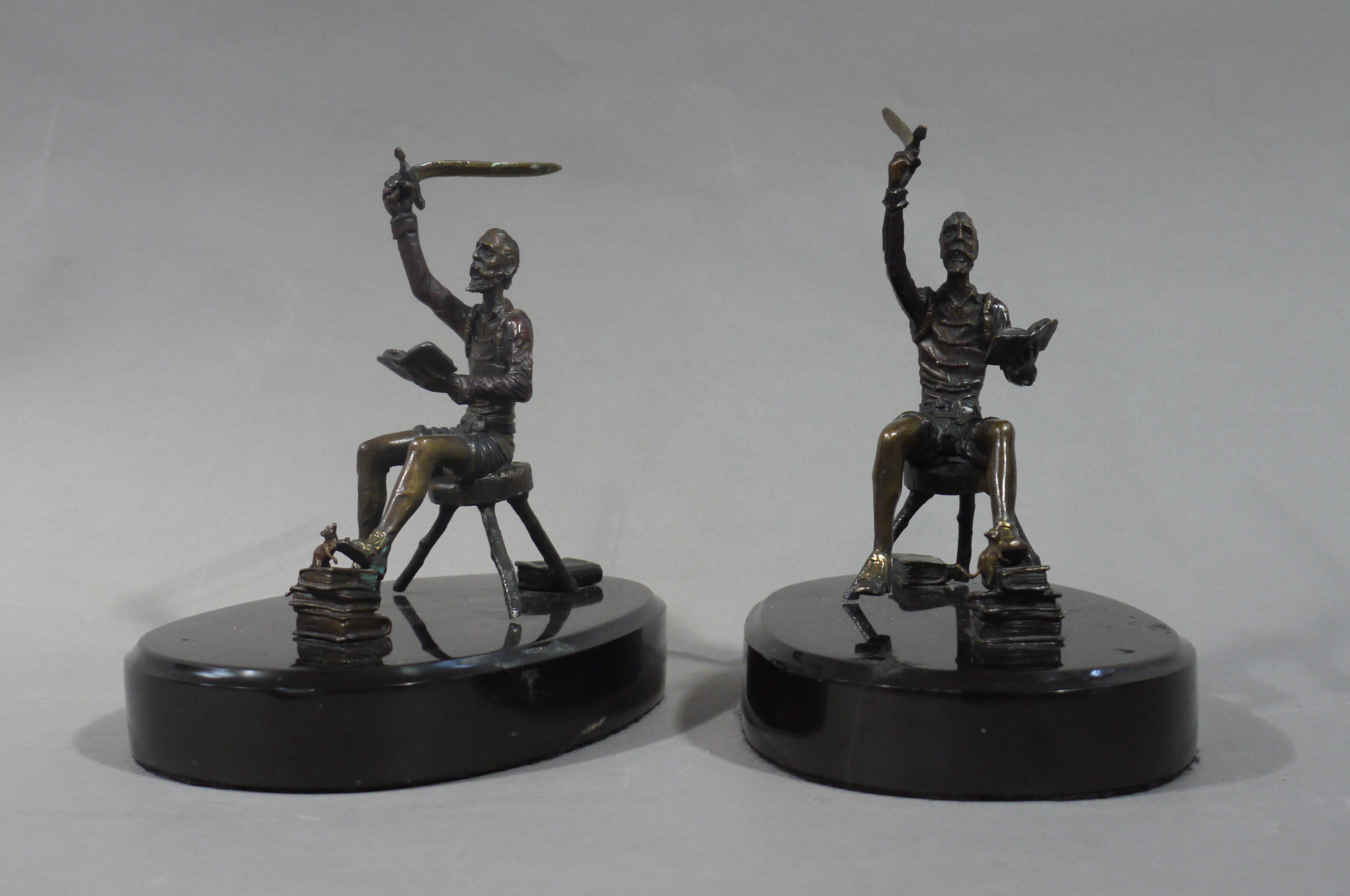 A pair of bronze sculptures of seated figures each reading a book in their left hand raising a