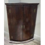 A George III oak hanging corner cupboard of shallow bow front form, dentil moulded cornice,