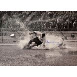 Sir Tom Finney Signed Print depicting Finney sliding through a waterlogged pitch in black and white,