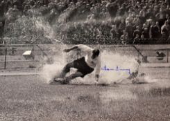 Sir Tom Finney Signed Print depicting Finney sliding through a waterlogged pitch in black and white,