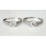 TWO CZ SINGLE STONE RINGS each with a central round cut stone flanked by diamond set shoulders,