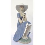 'NAO/LLADRO' FEMALE FIGURE wearing a wide brimmed hat and sitting on a stone wall,