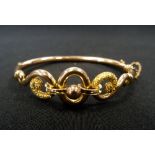 NINE CARAT GOLD BANGLE with textured scroll and circle design centrepiece, with safety chain,