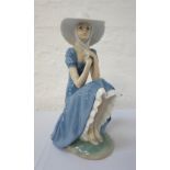 'NAO/LLADRO' FEMALE FIGURE wearing a wide brimmed hat and sitting a on a stone wall,