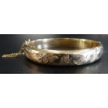 NINE CARAT GOLD HINGED BANGLE with floral engraved decoration and safety chain,