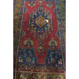 AN ANTIQUE WOOL RUG, the indigo and wine ground with central panel with palmettes,