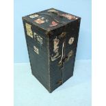 A black steamer trunk, opening to reveal a fitted interior with drawers and hanging space for