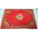 An Iranian hand-knotted tufted rug, with a central salmon pink medallion to a deep red field with
