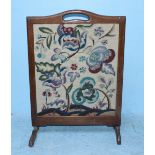 An oak framed embroidered fire guard decorated with floral motifs on a cream background