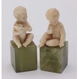 A pair of early 20th Century carved ivory figures of infant boys, each sat atop a green onyx