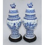 A pair of Delft blue and white pottery vases with covers, raised on pierced, turned wooden bases. (