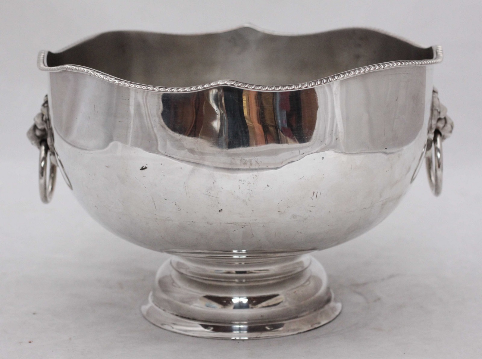 A large silver plated ice bucket with gadrooned shaped rim and lion mask handles on circular