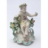 An 18th Century porcelain figure of a seated putti, in the Chelsea style, sitting amongst flowers