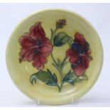 A Moorcroft pottery dish painted in the 'Hibiscus' pattern with pink flowers to a yellow ground,