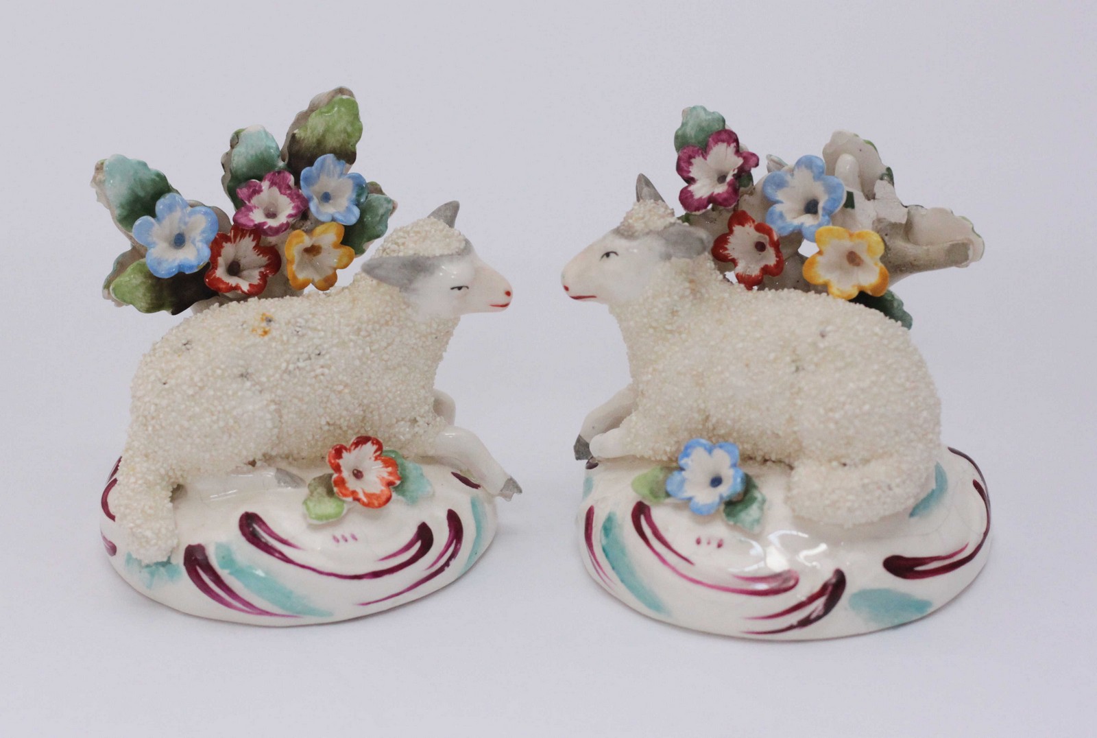 A pair of porcelain figures in the Chelsea style, modelled as recumbent sheep lying next to floral