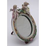 A Meissen porcelain oval easel mirror, surmounted with a pair of cherubs holding a floral swag and