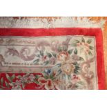 A large Chinese rug, with cream and green floral central and outer decoration to a red background,