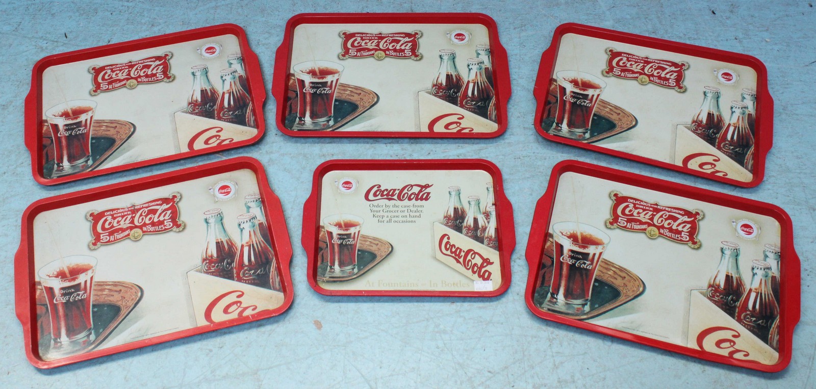 Five large advertising trays 'Coca-Cola 5c at fountains - in bottles 5c' and a smaller similar